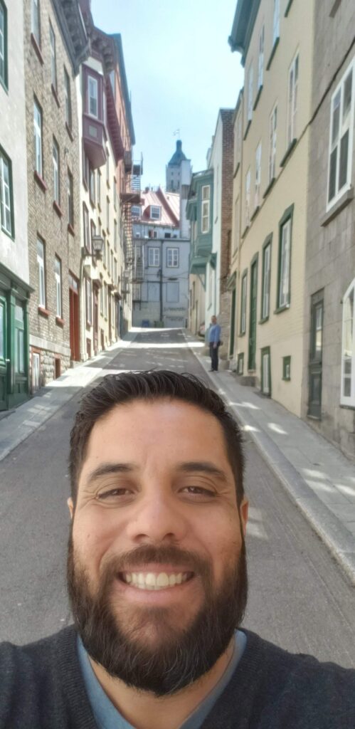Selfie de Alex Ferreira da Silva sorrindo em uma rua histórica da Cidade de Québec, Canadá.