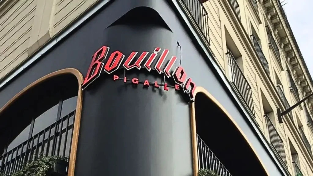 Close-up of the vintage art deco red neon sign of Bouillon Pigalle restaurant on a dark grey corner building in Paris, representing iconic cheap eats in Paris.