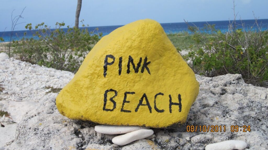 Pedra amarela sinalizando a Pink Beach em Bonaire, com mar azul ao fundo.